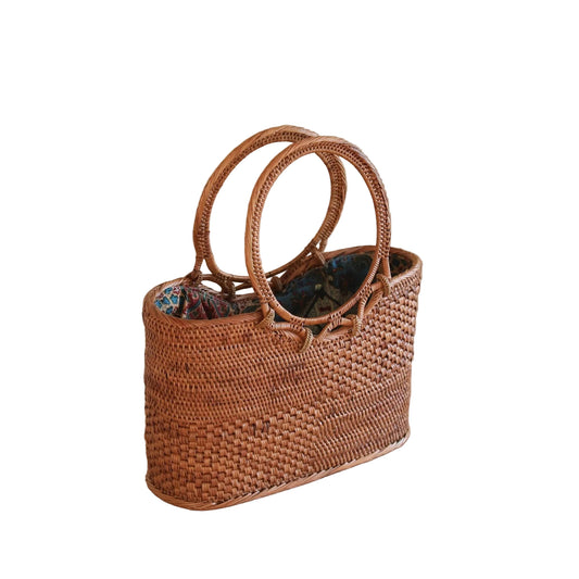 Woven handbag on a wooden surface with a plant in the background