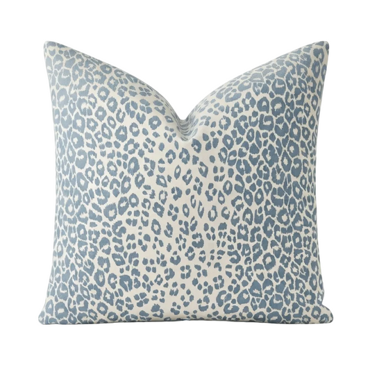 A square throw pillow featuring a blue leopard print pattern on a warm cream background, photographed against a clean white studio backdrop.