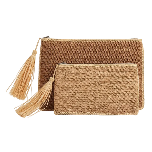 Two woven straw clutch bags in natural tan and light beige, featuring a larger rectangular bag and a smaller zippered pouch, both with matching tassels, set against a plain white background.