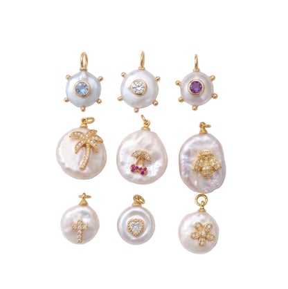 Nine gold and pearl pendants arranged in a 3x3 grid on a white background with soft diagonal shadows. The pendants feature various motifs including a palm tree, cherry, cross, flower, sun, and abstract shapes, embellished with small colored gemstones.