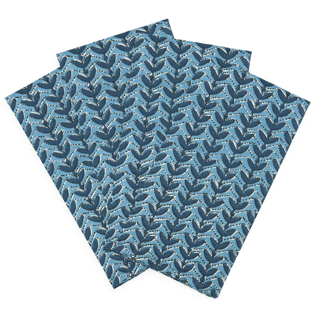 Block printed square fabric napkins with an allover repeating leaf pattern in shades of blue and navy on a white background.