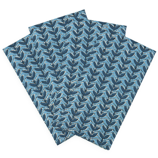 Block printed square fabric napkins with an allover repeating leaf pattern in shades of blue and navy on a white background.