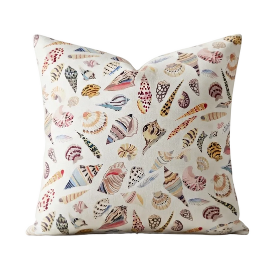 A square throw pillow featuring an all-over print of colorful seashells and sea urchins on a cream background, shown against a plain white studio backdrop.