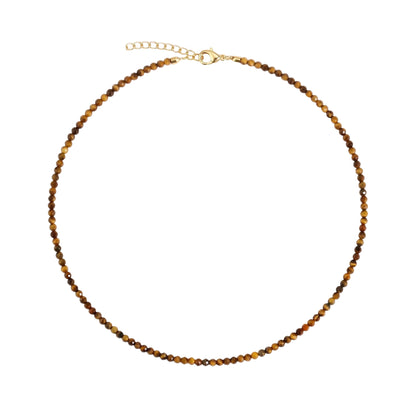 A beaded choker necklace with small brown and gold tiger's eye beads, a gold clasp, and a gold extender chain with a round tag, displayed on a clean off-white background with a Josephine brand logo in the bottom right corner.